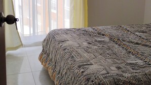 Un dormitorio con una colcha estampada, una ventana con cortinas amarillas y vistas a un edificio.