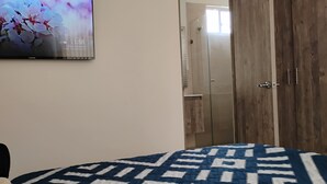 Un dormitorio con cama, armario y televisor empotrado mostrando un papel tapiz floral.