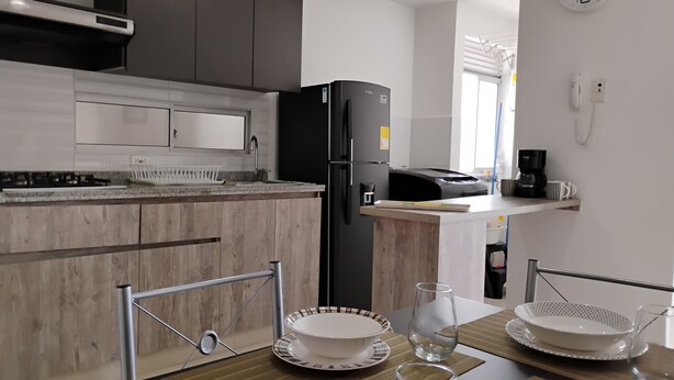 Una cocina moderna con un refrigerador negro, una cafetera y un comedor con una mesa dispuesta para dos personas.