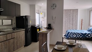 Una cocina funcional con electrodomésticos modernos, un comedor con mesa y sillas de madera, y un dormitorio con colcha estampada.