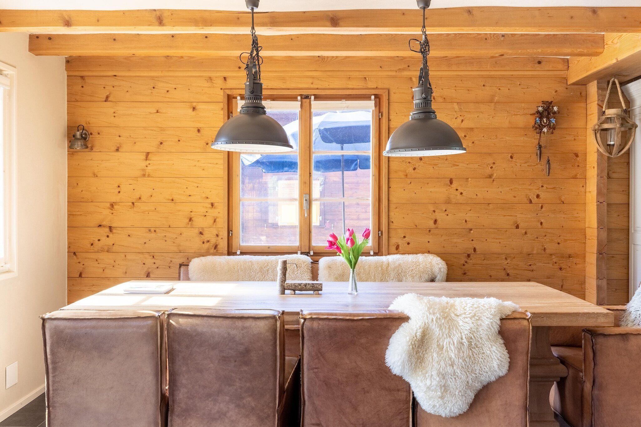 Une pièce aux murs lambrissés, comprenant une table à manger, des chaises et deux lampes suspendues.