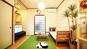 Ein gemütlicher Wohnbereich mit Fernseher, Sofa, kleinem Tisch, einem Panda-Plüschtier und einem Blumentopf.