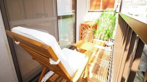 Ein Holzstuhl mit weißem Kissen, ein kleiner Holztisch und ein Blumentopf auf einem Balkon.