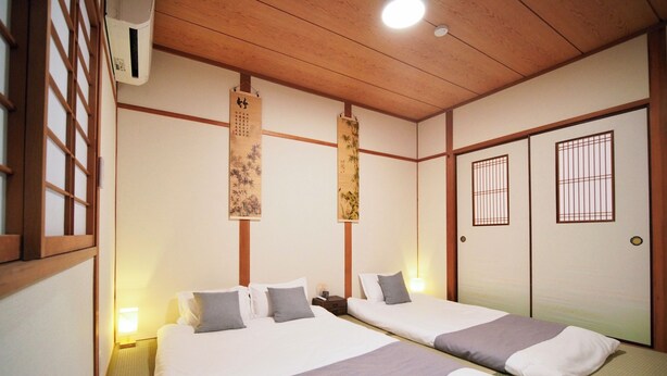 Ein traditionell eingerichteter japanischer Raum mit zwei Betten, Holzbalken, Tatami-Böden und verschiebbaren Türen.