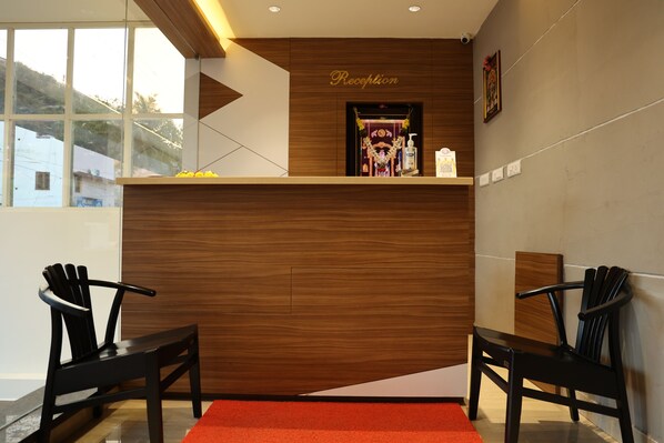 A reception area with a wooden reception desk, two black chairs, a red carpet, and a wall-mounted sign that reads "Reception".