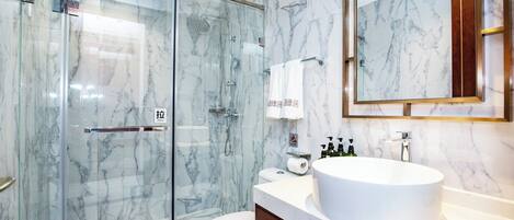 A modern bathroom with a glass-enclosed shower, a white toilet, and a large oval sink with a mirror above it.