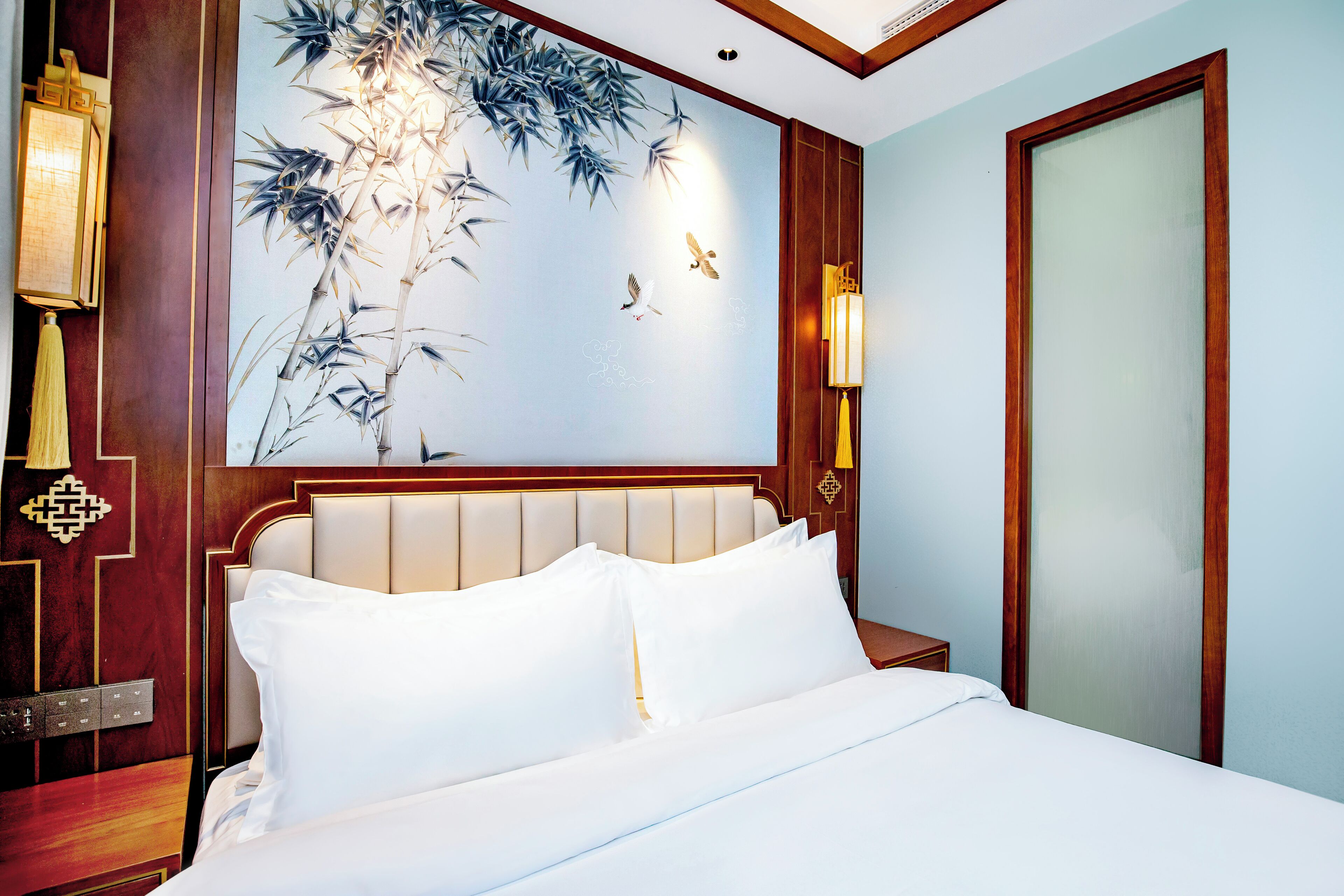 Quarto de hotel com cama, um mural na parede e porta de madeira.