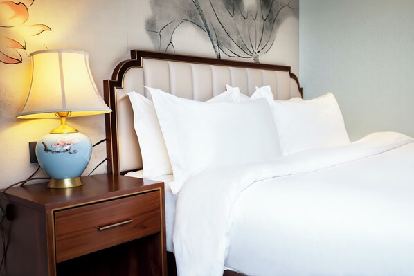 A neatly made bed with white linens, a wooden nightstand with a lamp, and a wall art piece.