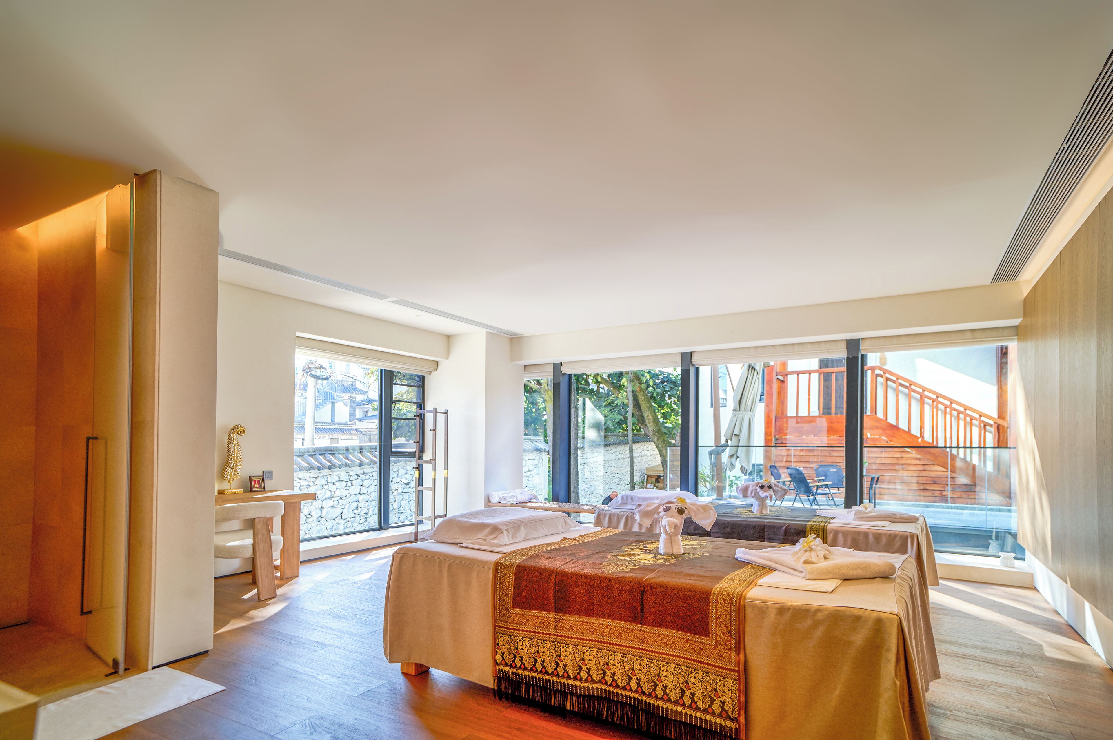 A spacious room with a large bed, a massage table, and a view of a staircase and outdoor area.