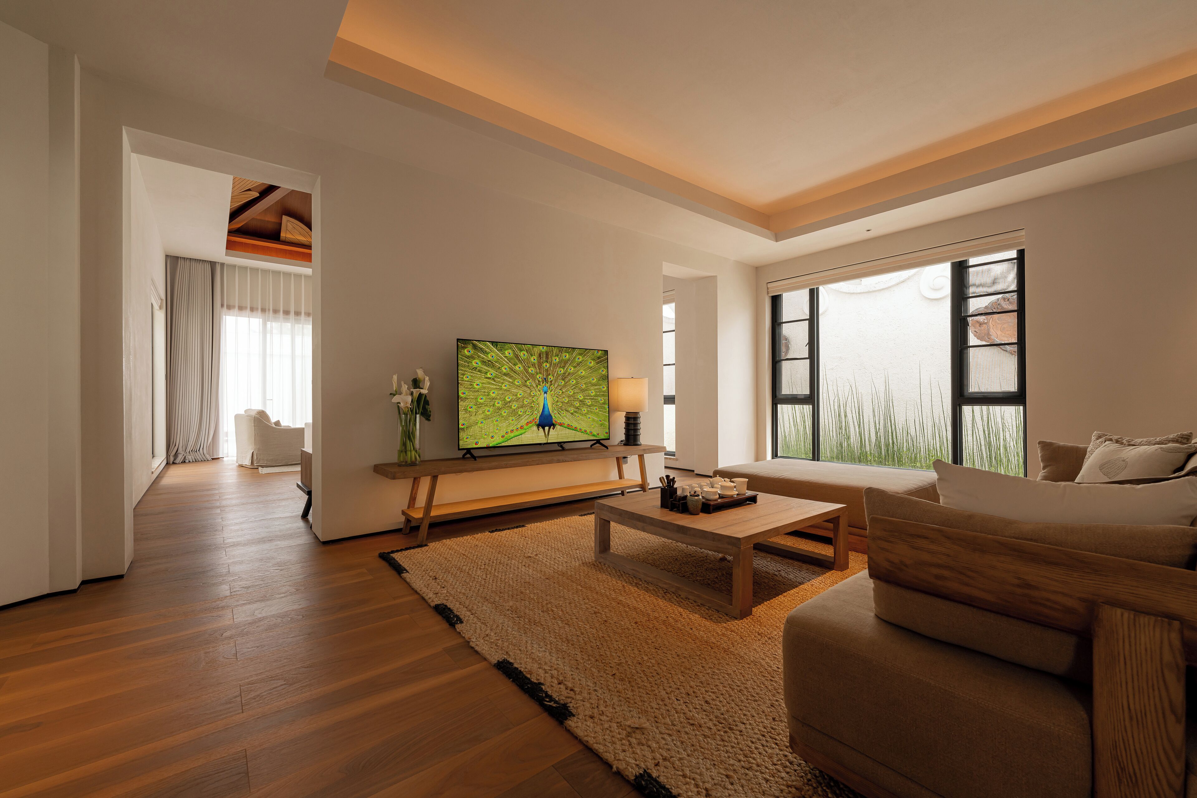 Een moderne woonkamer met een houten vloer, een beige bank, een salontafel en een flatscreen televisie waarop een pauw te zien is.