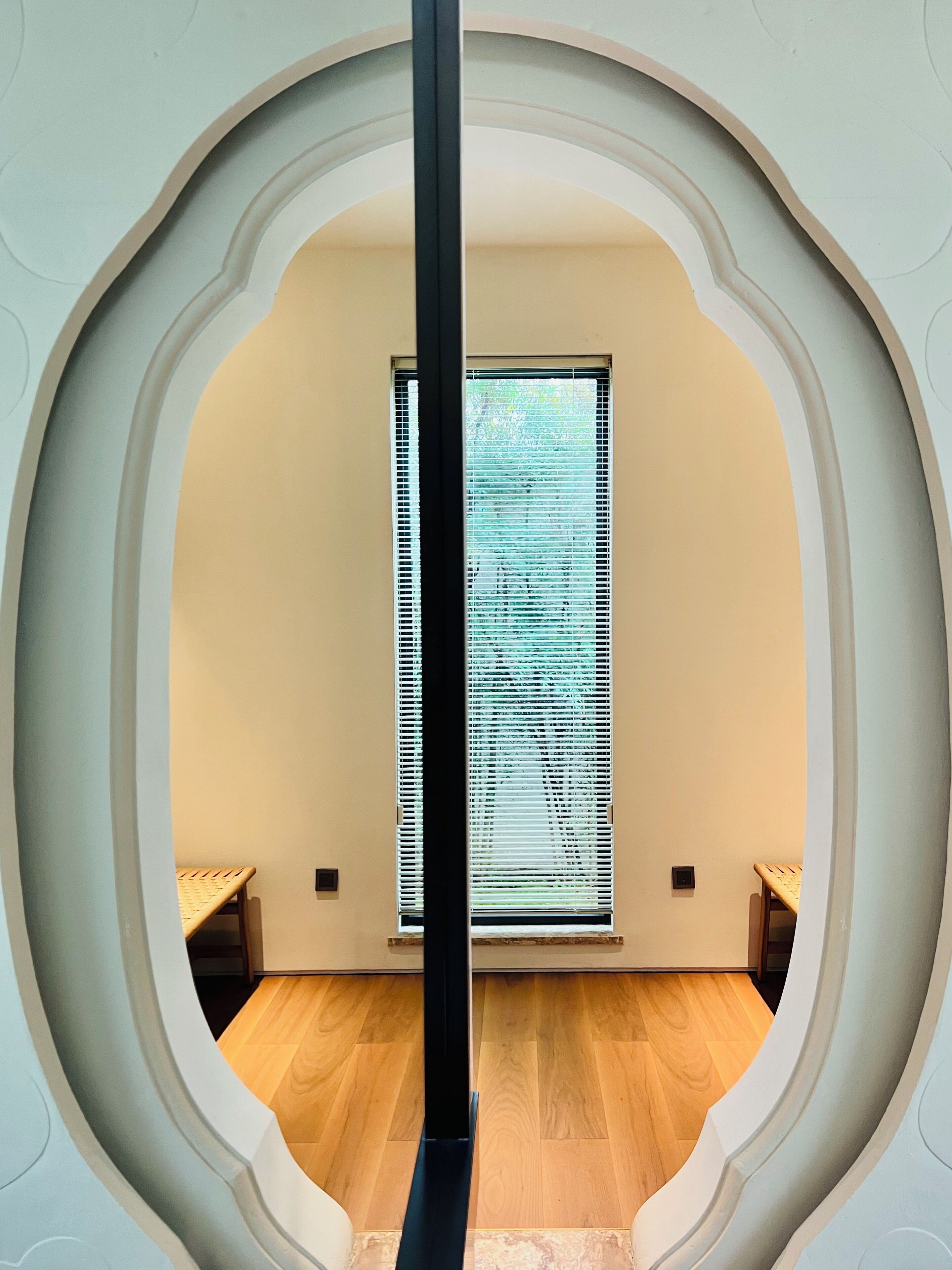 Una habitación con piso de madera, una ventana con persianas y una pared blanca con un arco decorativo.