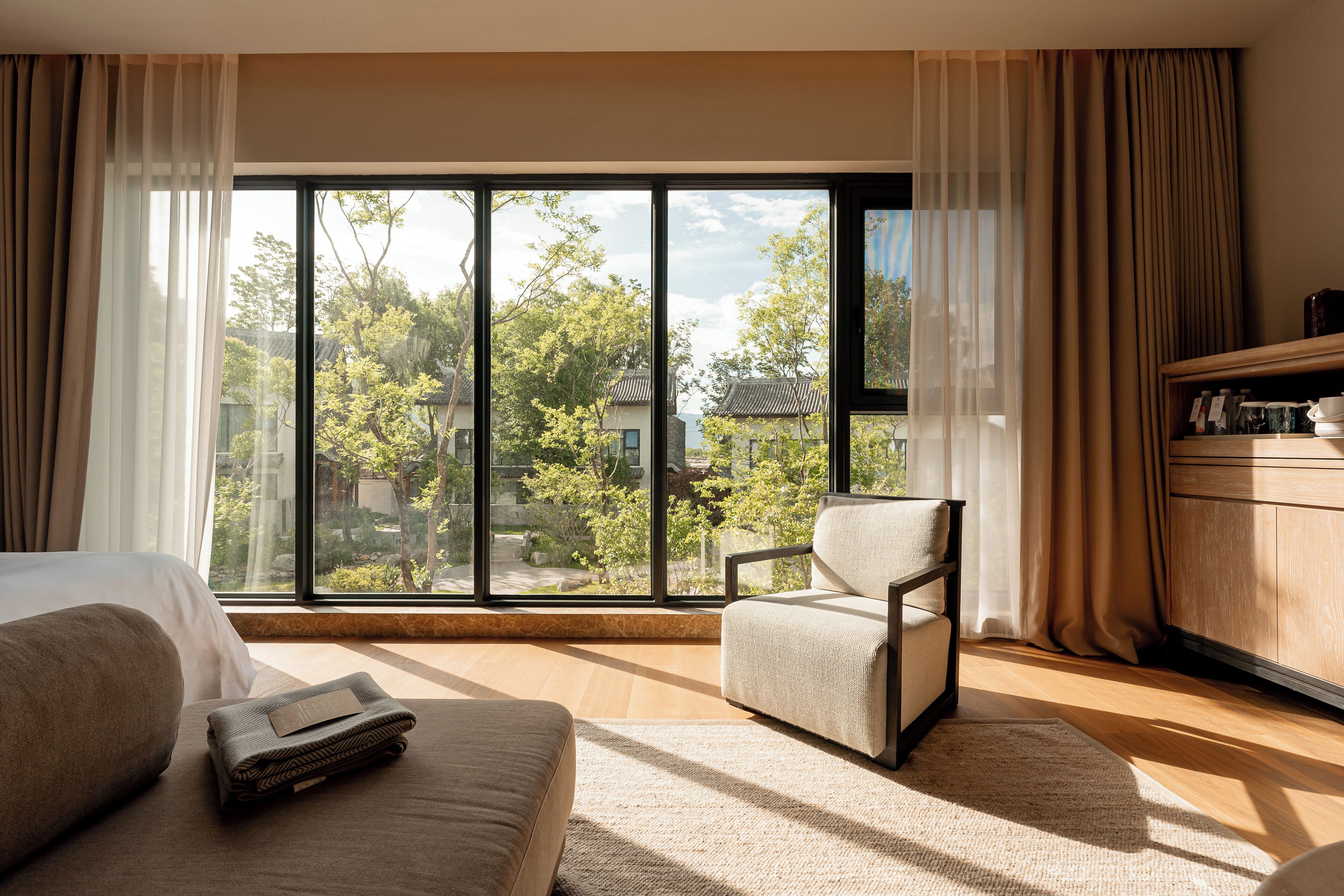 Une chambre d’hôtel avec une grande fenêtre, un canapé, un fauteuil et un meuble en bois.
