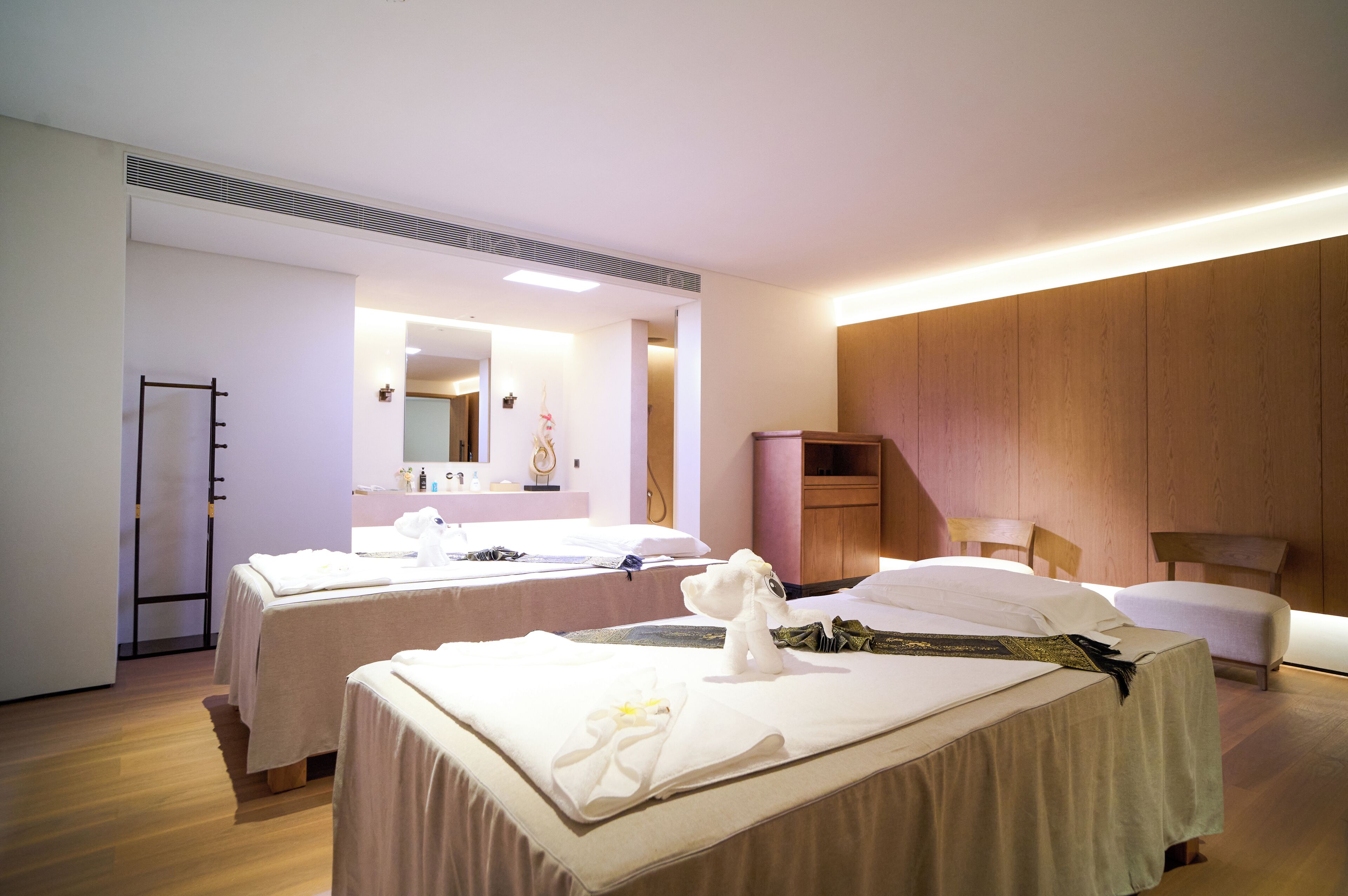 A hotel room with two beds, a wooden wardrobe, a mirror, and a bedside table.