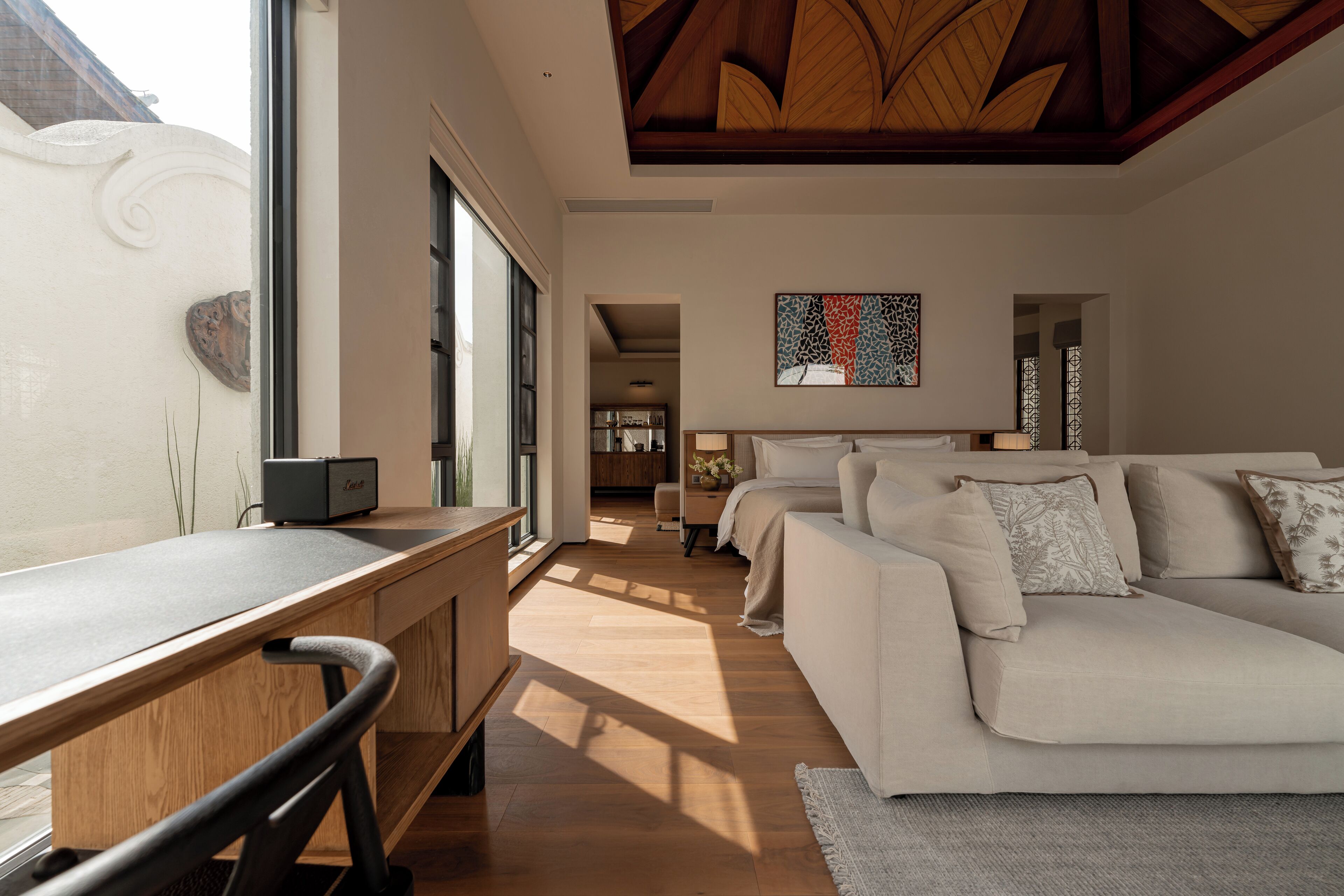 A modern living room with a wooden desk, a beige sofa, and a large window.
