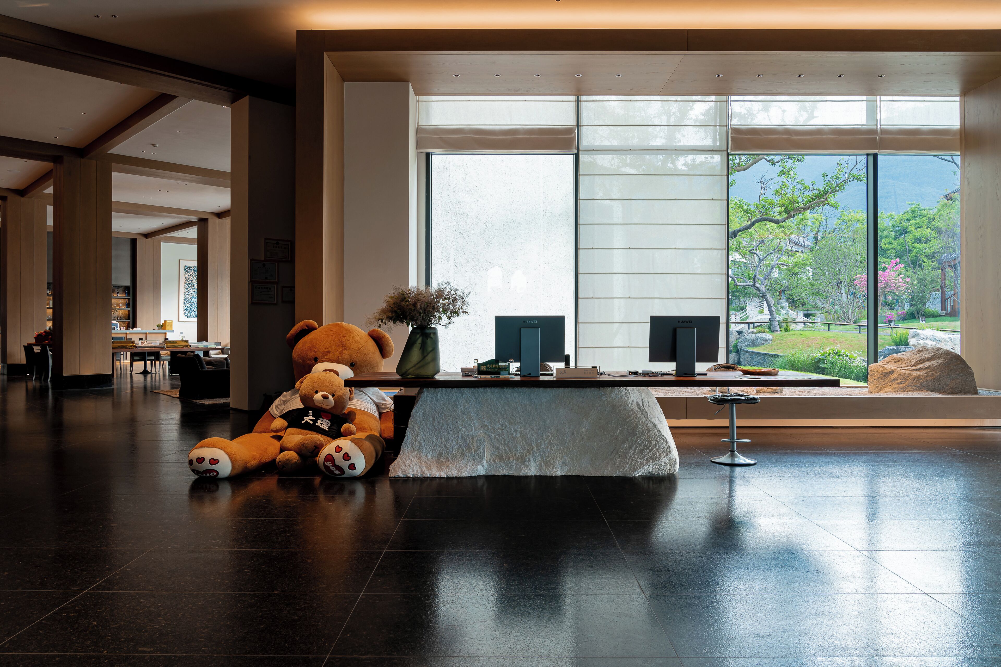 A modern hotel lobby with a large window, a reception desk, and a teddy bear on the floor.