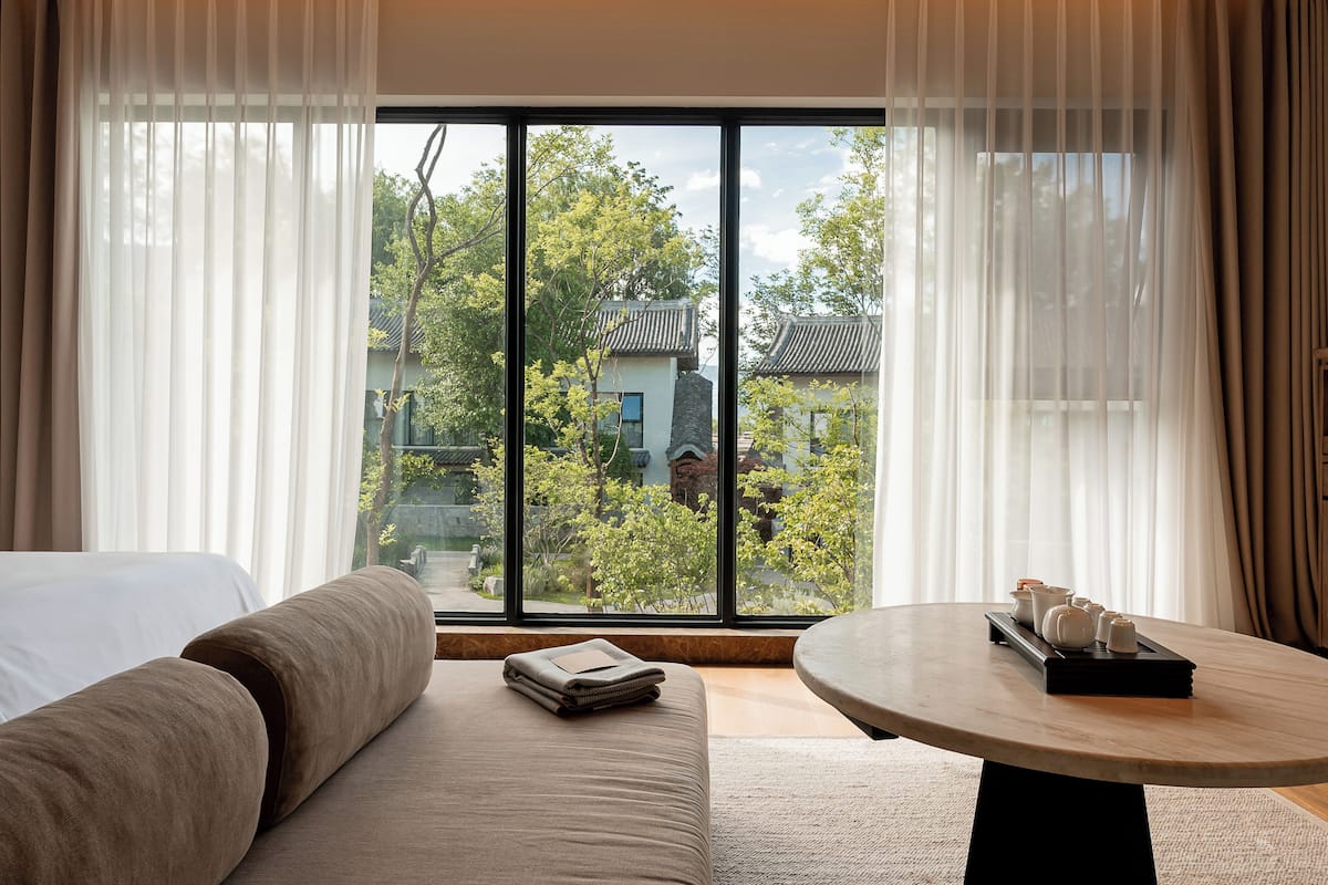 A hotel room with a large window, a bed, a sofa, and a round table with tea set.