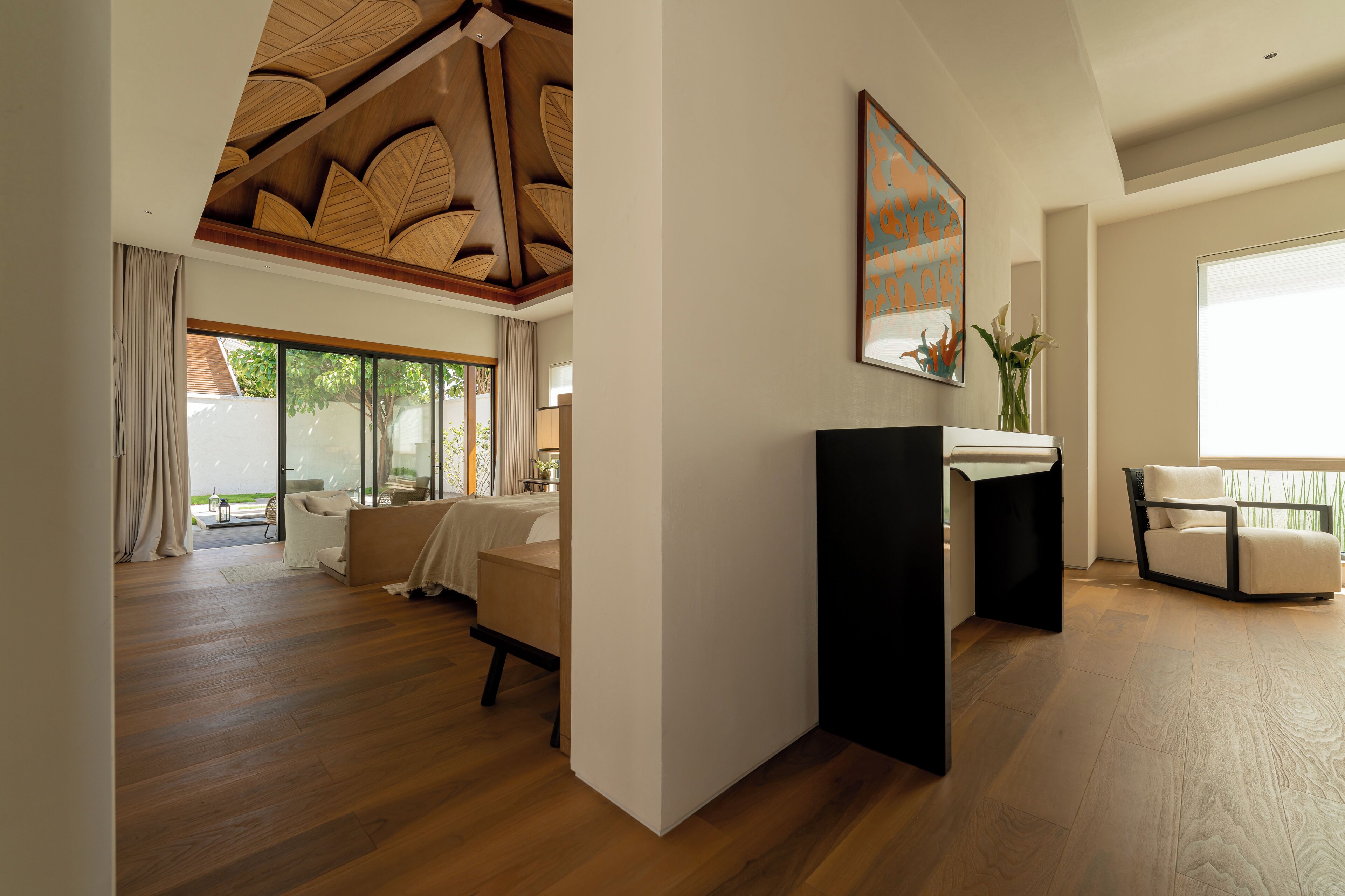 Uma sala ampla com teto de madeira, uma janela grande, um sofá, uma mesa de centro e uma mesa lateral com um vaso.