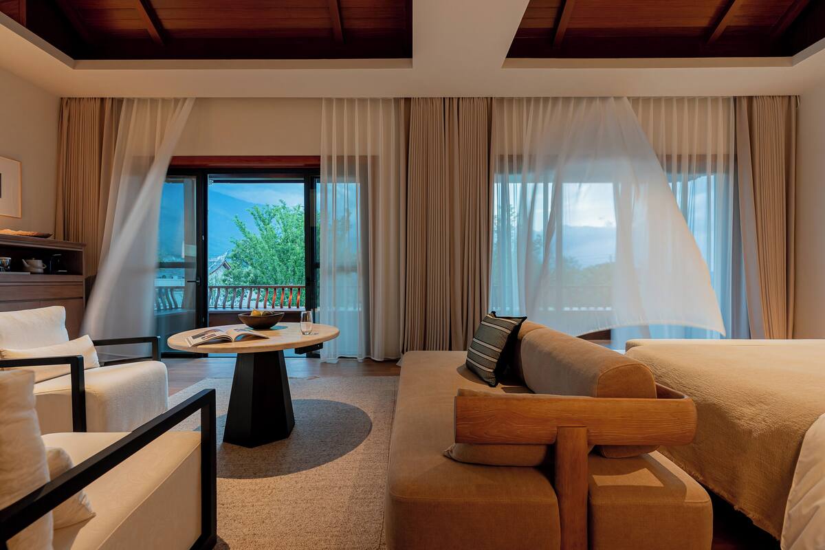 A hotel room with a sofa, a dining table, and a view of the outdoors.