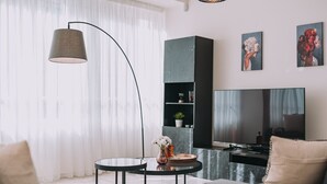 Un salon moderne comprenant un canapé, deux tables basses, une lampe sur pied, un téléviseur et des œuvres d’art accrochées au mur.