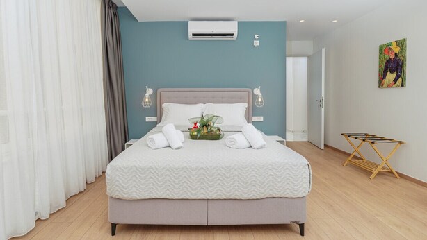 Une chambre moderne avec un lit, des rideaux, un appareil de climatisation, un tableau et une chaise pliante.