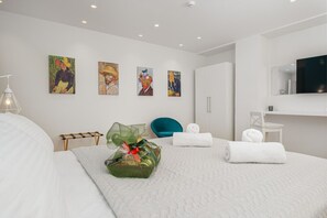 Ein modernes Hotelzimmer mit einem großen Bett, einer Sitzecke mit einem Sessel, einem kleinen Tisch und Kunstwerken an den Wänden.