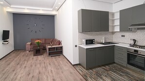 Une cuisine moderne avec des meubles gris, un four à micro-ondes et un four encastré. Le salon est doté d'un canapé gris et d'un vase de fleurs.
