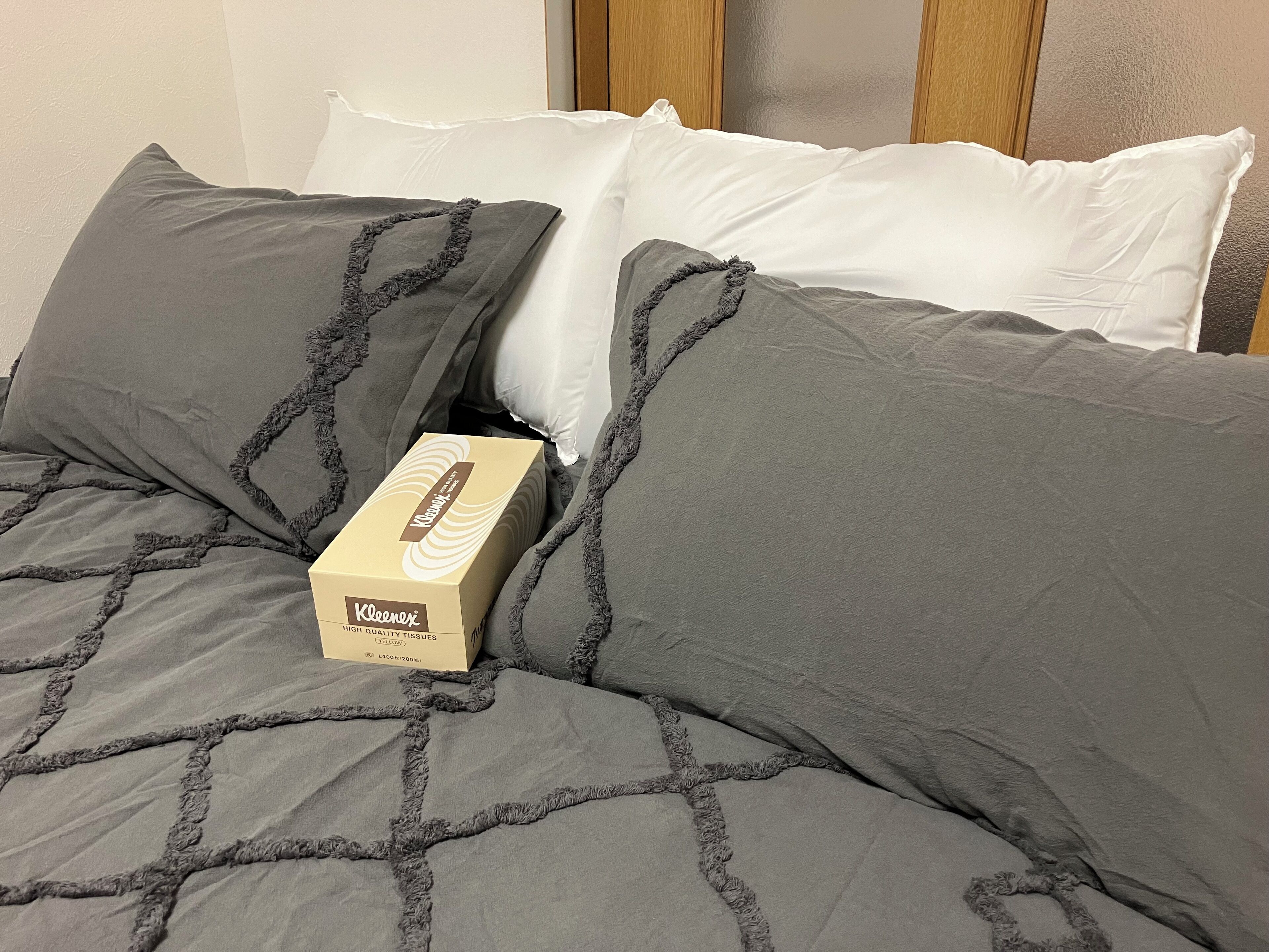 Ein Bett mit grauer Bettwäsche und einer Tasche Taschentücher.