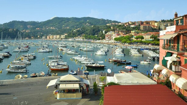 Un port de plaisance où sont amarrés de nombreux bateaux, un petit kiosque et des bâtiments dotés de balcons.