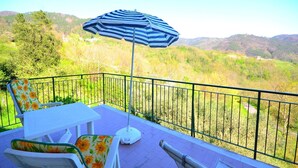 Un balcon donnant sur un paysage vallonné, un parasol à rayures et du mobilier d’extérieur.