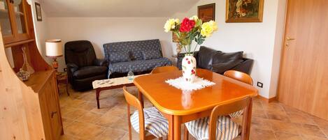 A dining area with a wooden table, chairs, a vase with flowers, a sofa, and a cabinet.