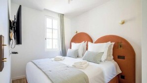 Habitació d'hotel amb llit, televisió penjada a la paret i finestra amb cortines.