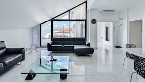 Un salón moderno con una mesa de centro de vidrio, un sofá de cuero negro y un amplio ventanal con vistas a edificios.