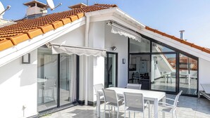 Una terraza moderna en la azotea con zona de comedor, puertas de cristal y vistas de los edificios circundantes.