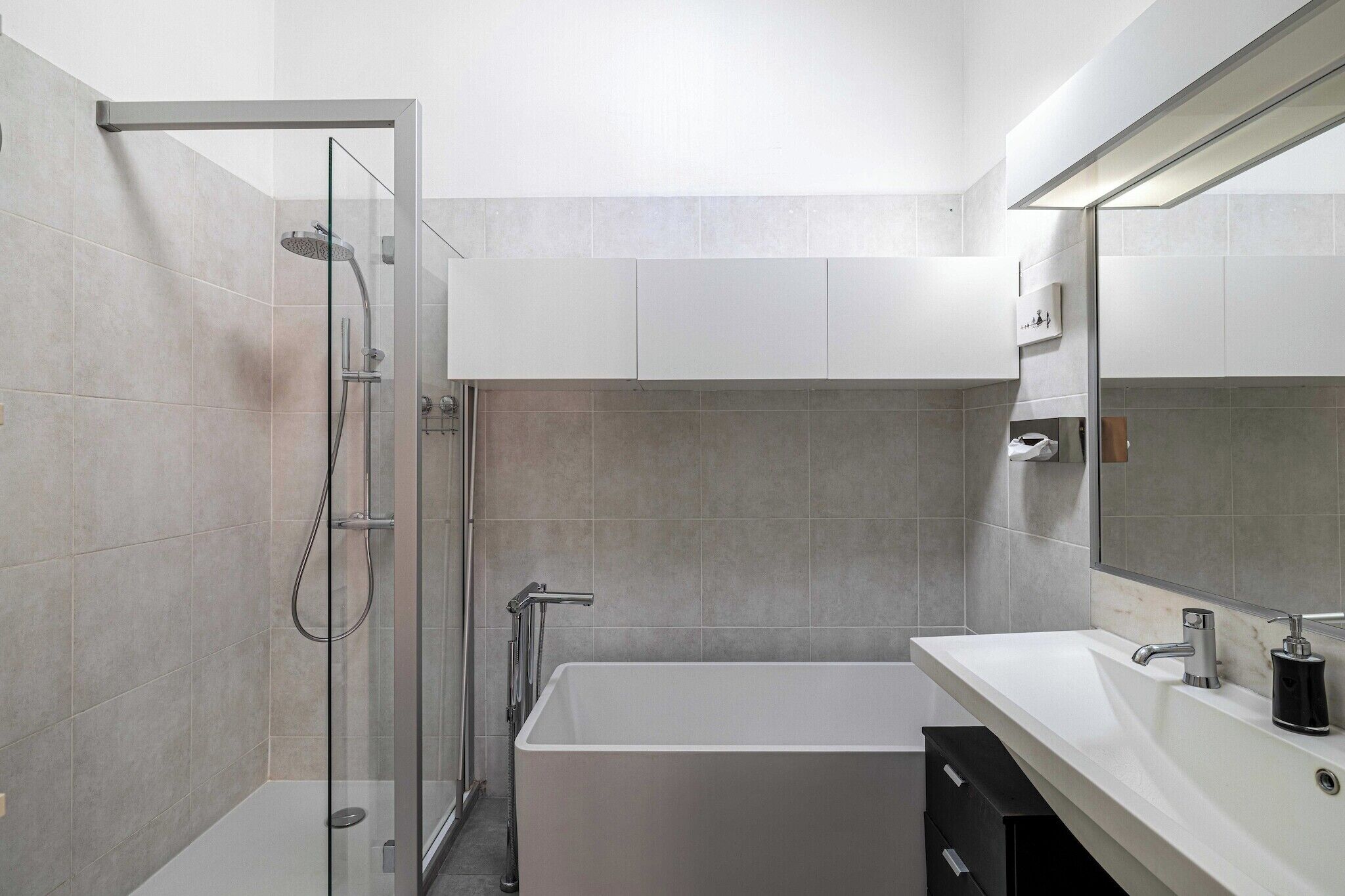 A modern bathroom with a glass-enclosed shower, a white bathtub, and a large mirror above the sink.
