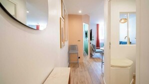 Un pasillo estrecho con piso de madera, un banco blanco, una silla y un inodoro blanco.