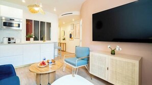 Una sala moderna con televisor de pantalla plana, un comedor con mesa redonda y una cocina con microondas y armarios.