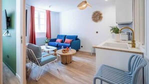 Una sala de estar moderna con un sofá azul, una mesa de centro redonda y un comedor con una mesa y sillas blancas.