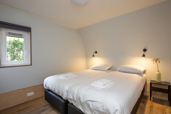A bedroom with a bed, two bedside lamps, a nightstand, a vase with flowers, and a window with blinds.