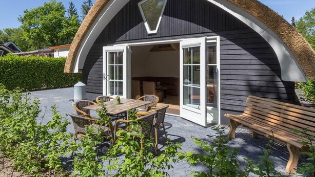 Ein modernes Haus mit einem Strohdach, einer offenen Terrasse mit Gartenmöbeln und Blick auf die Umgebung.