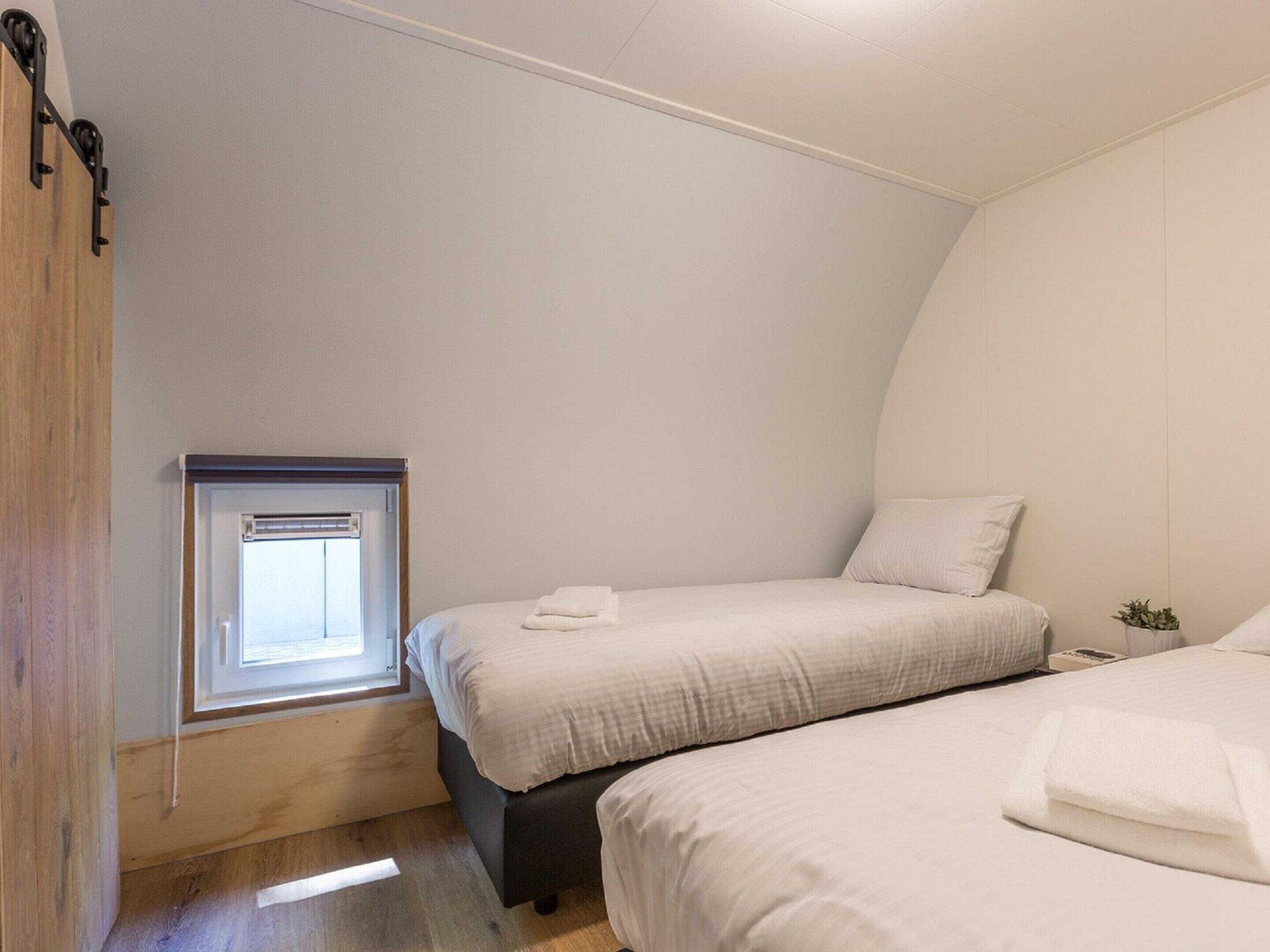 Ein Schlafzimmer mit zwei Betten, einem kleinen Fenster und einer Holztür.