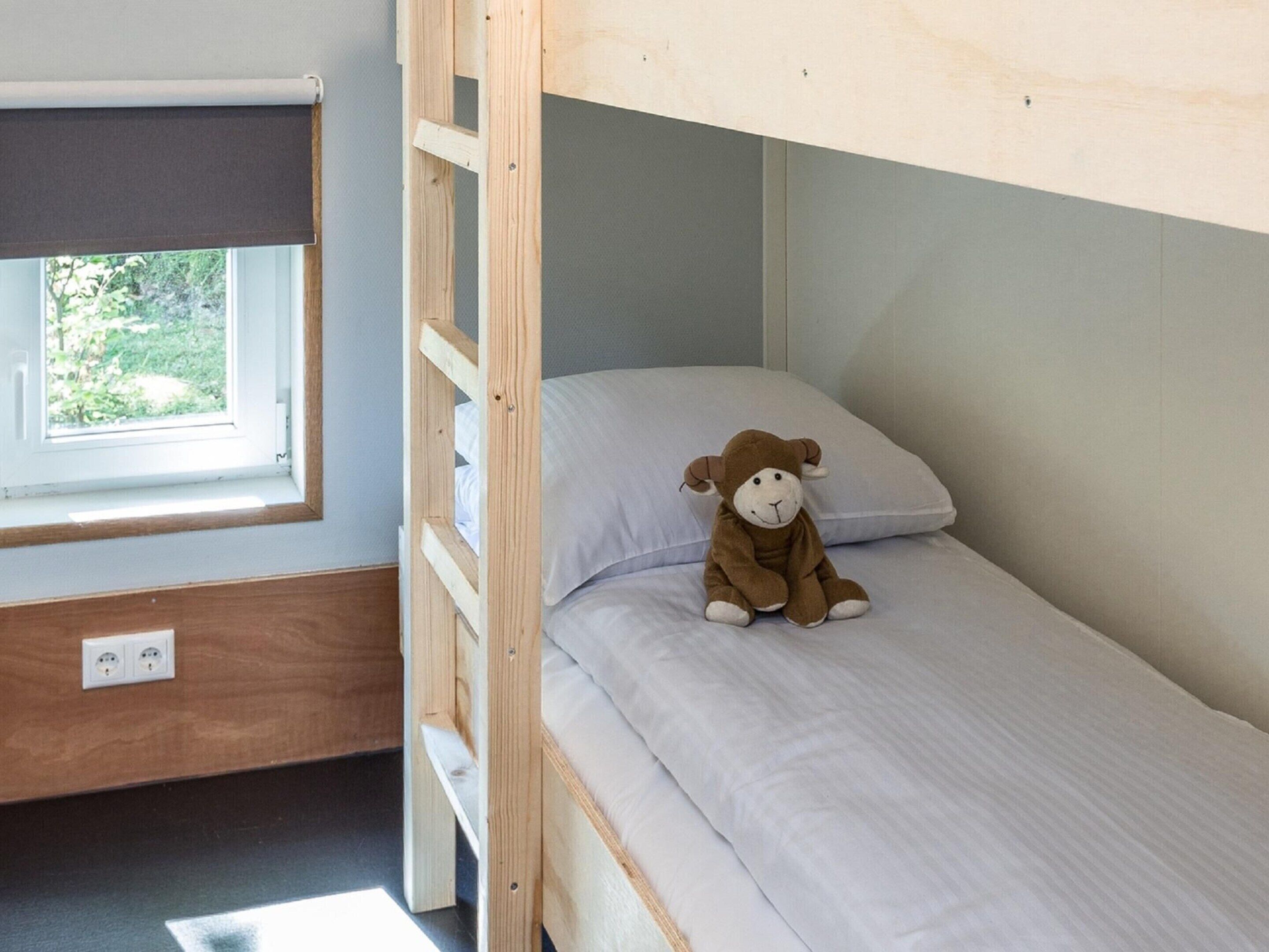 A bunk bed with a window, a power outlet, and a stuffed monkey toy on the bed.