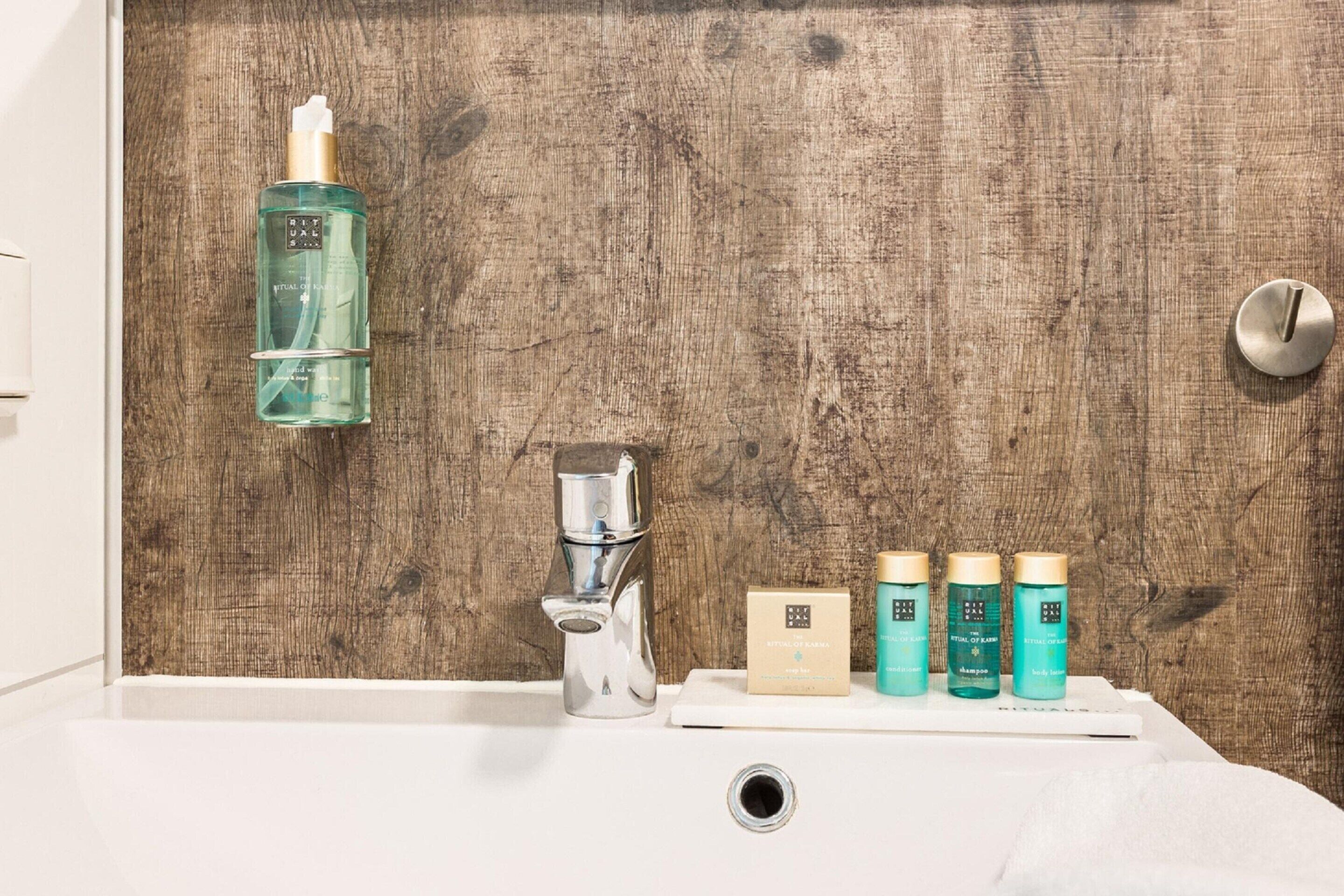 A bathroom with a wooden wall, a sink, a faucet, and three bottles of shampoo.