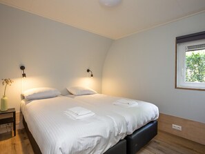 A bedroom with a bed, two bedside tables, a window with a view, and a wall-mounted light fixture.