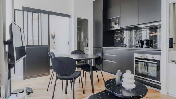 Une cuisine moderne avec des meubles de couleur sombre, un four encastré et un coin repas comprenant une table ronde et des chaises.