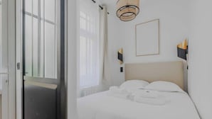 Une chambre à coucher moderne avec un grand lit, une table de chevet, une lampe fixée au mur et une fenêtre avec des rideaux.