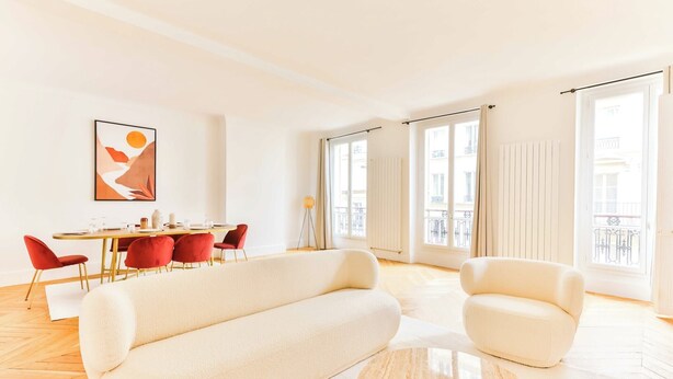 A modern living room with a sofa, chairs, a dining table, and a large window.