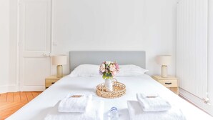 A neatly made bed with white linens, a vase of flowers, and two bedside lamps on wooden nightstands.