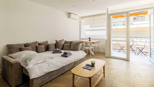 A modern living room with a sofa, a small table, and a balcony with outdoor seating.