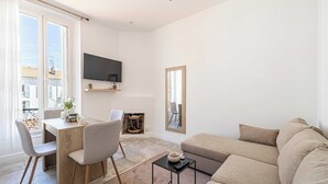 Un salon moderne comprenant un canapé, une table à manger avec des chaises, un téléviseur fixé au mur et un grand miroir.