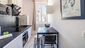 Une cuisine compacte avec un plan de travail noir, un évier et un coin repas avec deux chaises. Un panneau d’accueil est visible sur le plan de travail.